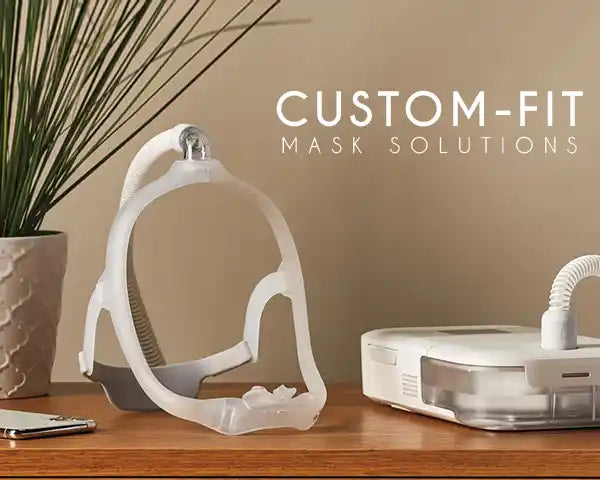 Custom-fit mask solutions displayed on a wooden table with a plant, phone, and CPAP machine, highlighting the personalized mask design for comfort and functionality.