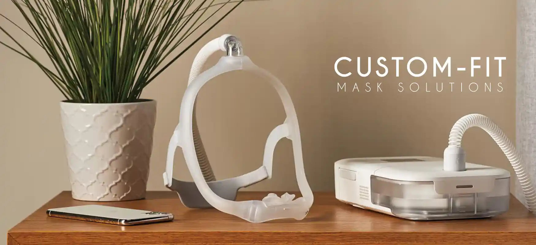 Custom-fit mask solutions displayed on a wooden table with a plant, phone, and CPAP machine, highlighting the personalized mask design for comfort and functionality.